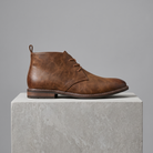 Men's full-grain leather lace-up chukka boots in brown, straight-on gray pedestal shot