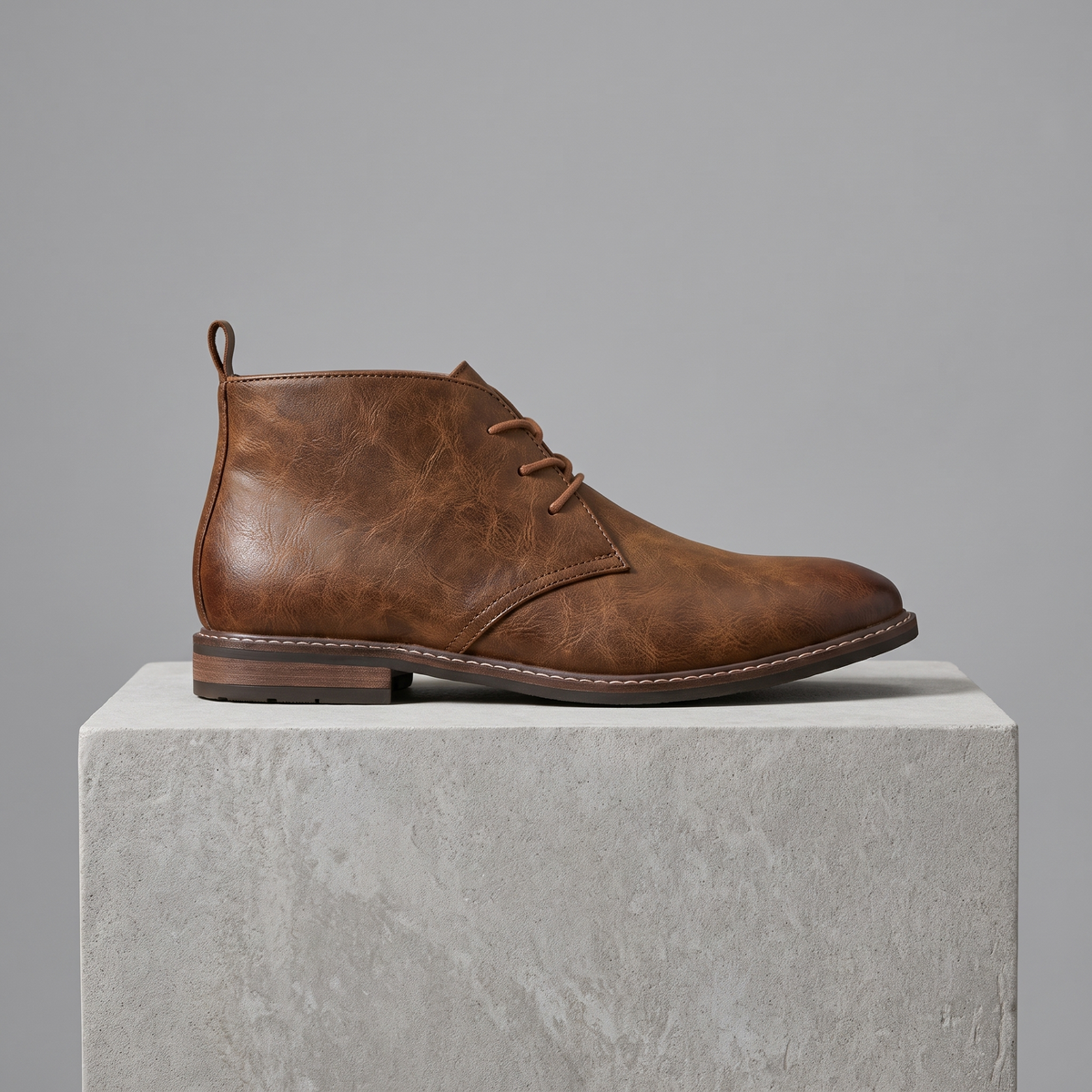 Men's full-grain leather lace-up chukka boots in brown, straight-on gray pedestal shot